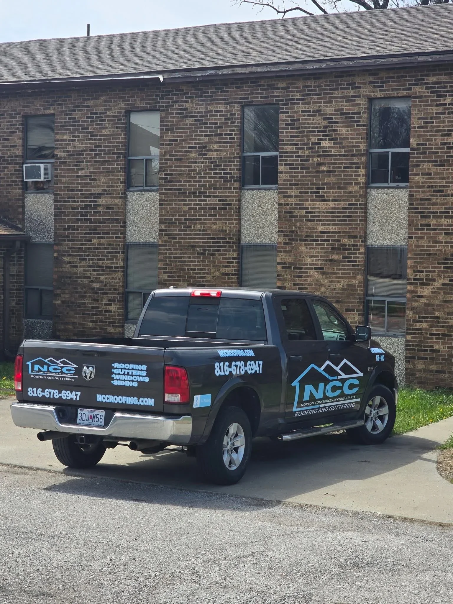 Service truck parked in front of brick building with asphalt shingle roof