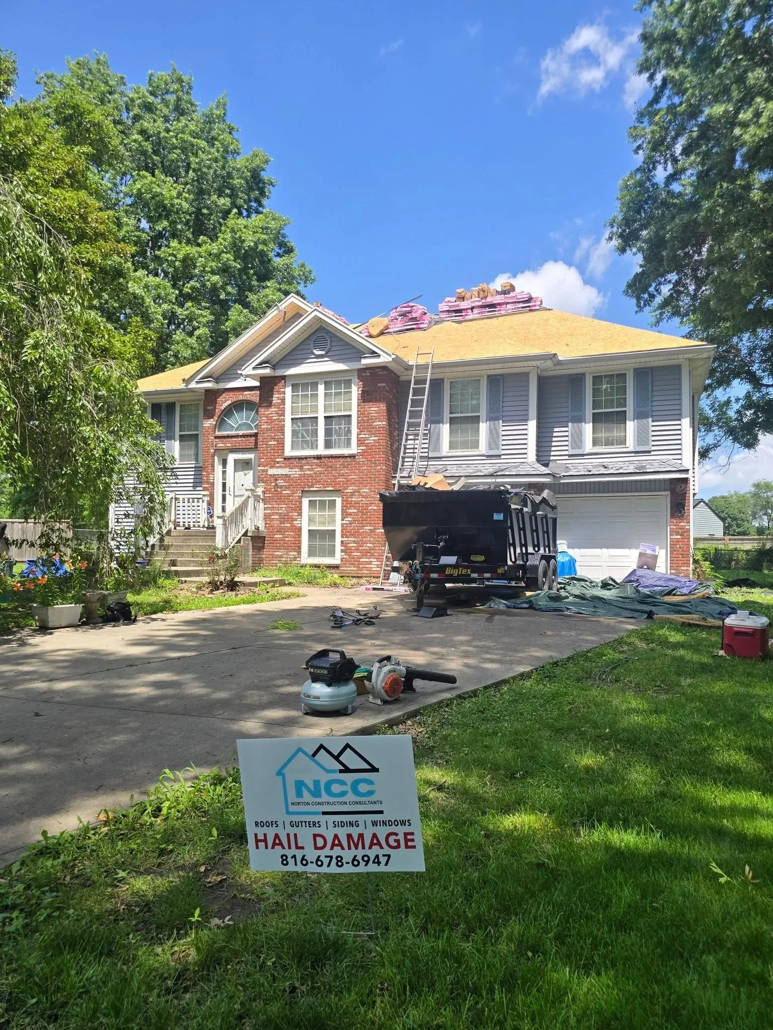 Two-story brick home with new yellow asphalt shingles, roofing equipment and materials on roof during replacement